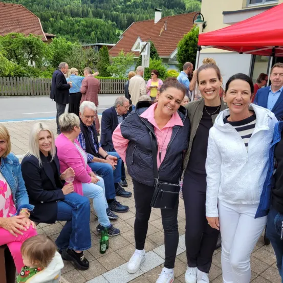 Mehrere Erwachsene und ein Kind versammeln sich draußen in einer malerischen Gegend, einige sitzend und andere stehend, mit einem Zelt im Hintergrund.