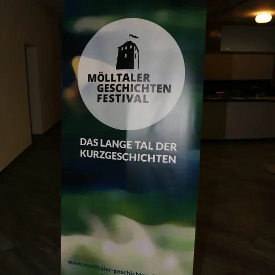 Ein Schild für das Molltaler Geschichten Festival mit einer Gebäudeillustration und einer Website-Adresse.