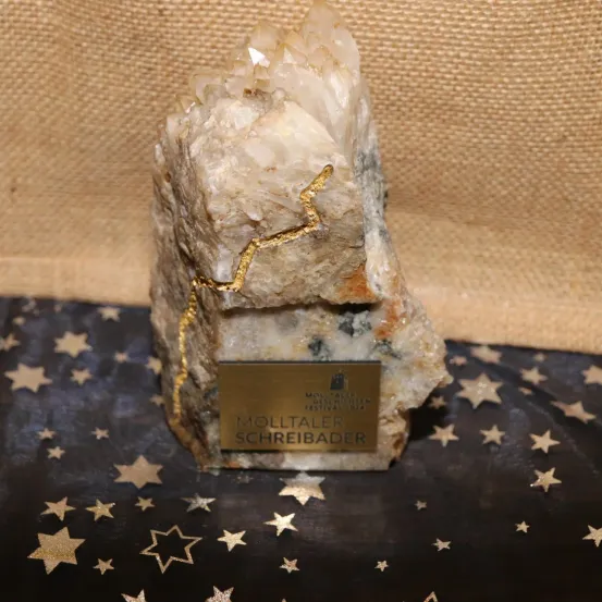 Ein großer Kristallfelsen mit goldenen Akzenten ruht auf einem Stoffhintergrund mit Sternen. Unter dem Felsen befindet sich eine Plakette mit dem Text 'MOLLTALER SCHREIBADER'.