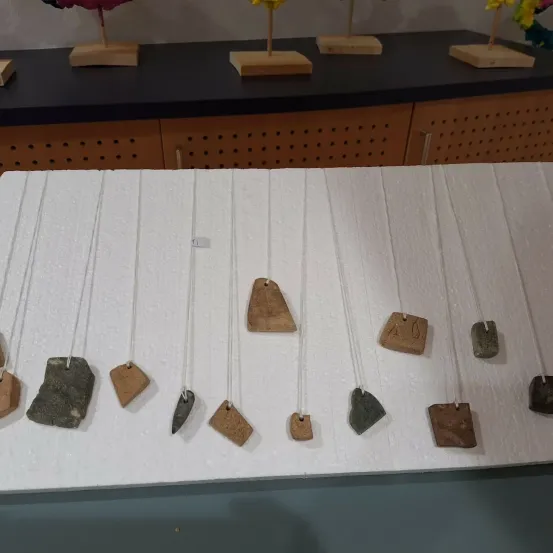 Eine Ausstellung verschiedener Steinanhänger auf einer weißen Oberfläche, jeder mit einem Holzständer, und ein schwarzer Tisch mit Löchern im Hintergrund.