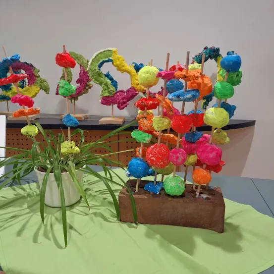 Eine Ausstellung bunter, mehrfarbiger Lollipops auf Stöcken, die auf einem Tisch angeordnet sind, mit einer Topfpflanze in der Nähe und einer schlichten weißen Wand im Hintergrund.