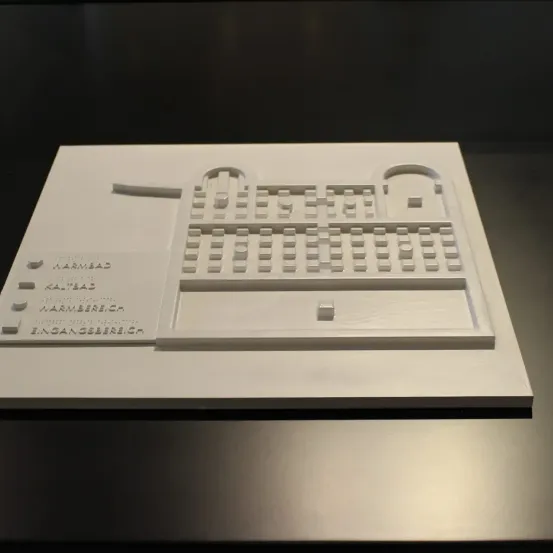 Ein weißes Architekturmodell wird auf einer schwarzen Oberfläche ausgestellt. Das Modell weist Bezeichnungen wie 'Warmbad', 'Kaltbad' und 'Warmbaderei' auf. Das Design besteht aus mehreren Bereichen, die möglicherweise verschiedene Zonen eines Gebäudes darstellen.