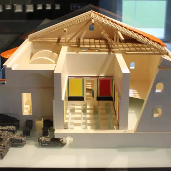 Ein Modell eines alten römischen Hauses mit gefliestem Dach und farbenfrohen Türen, ausgestellt auf einer weißen Oberfläche.