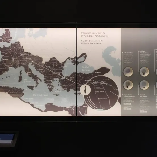 Ein Lehrposter, das eine Karte des Römischen Reiches am Beginn des 21. Jahrhunderts n. Chr. zeigt. Verschiedene Regionen und Meere sind beschriftet, zusammen mit bemerkenswerten Städten und Sehenswürdigkeiten.