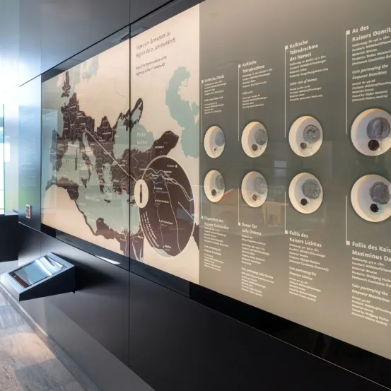 Eine Wandmontage mit Karte und Text, die das Römische Reich und römische Straßen zeigt. Es sind mehrere Münzen ausgestellt, jede mit begleitenden Informationen.