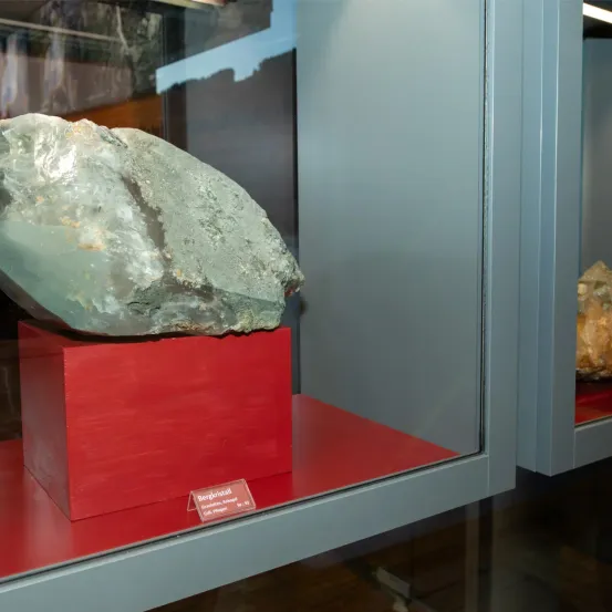 Ein großer, klarer grüner Mineral namens Berylkristall wird in einem Museum ausgestellt. Das Mineral befindet sich auf einem roten Kasten mit einem Etikett.