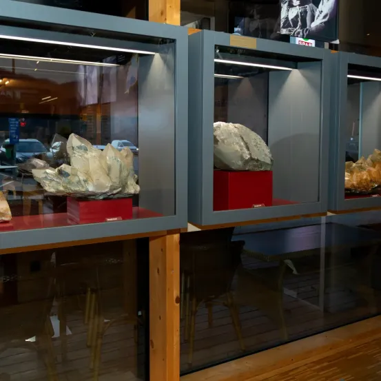 Drei Glasvitrinen mit großen Kristallen in einem Geschäft ausgestellt. Eine Vitrine hat einen großen Kristall auf einem roten Sockel.