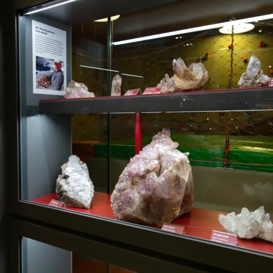 Eine Vitrine mit Mineralien und Kristallen, ein Plakat mit Text und einem Mann in einem Hut.