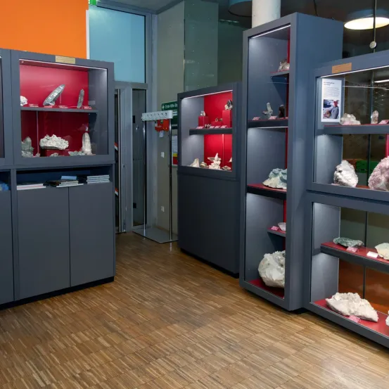 Ein Raum mit Holzböden und mehreren grauen Schränken, die Mineralien auf roten Regalen ausstellen.