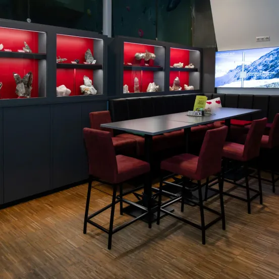 Ein Essbereich mit roten Stühlen und einem Tisch in einem Raum mit Holzboden. Der Raum hat Schränke mit roter Beleuchtung und Displays von Steinen.