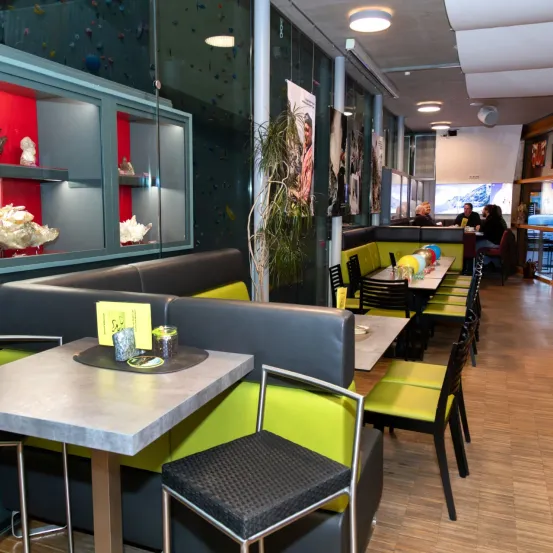 Das Innere eines Restaurants mit grauen und gelben Sitzbänken, Holzböden und einem Tisch mit einem gelben Menü. Vitrinen und Kunst sind an der Wand zu sehen.