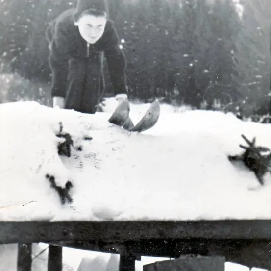 Ein junger Mensch in Winterkleidung beugt sich über einen schneebedeckten Tisch und untersucht etwas auf der Oberfläche.