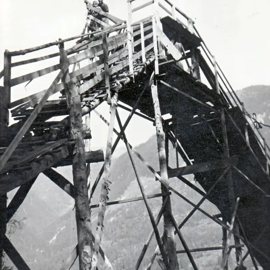 Ein Schwarz-Weiß-Bild einer Person auf einer Holzstruktur mit einem Gebirgshintergrund.