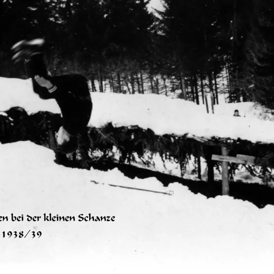 Ein Skifahrer führt einen Sprung über einen schneebedeckten Hügel in einem Berggebiet aus, datiert 1938/39.