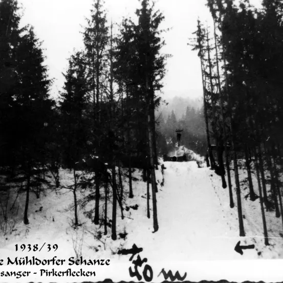 Schwarz-Weiß-Bild von 1938/39 zeigt einen verschneiten Wald mit Bäumen. Eine Person geht auf einem schneebedeckten Pfad. Es steht 'Mühldorfer Schanze' und 'Pirkerflecken'.