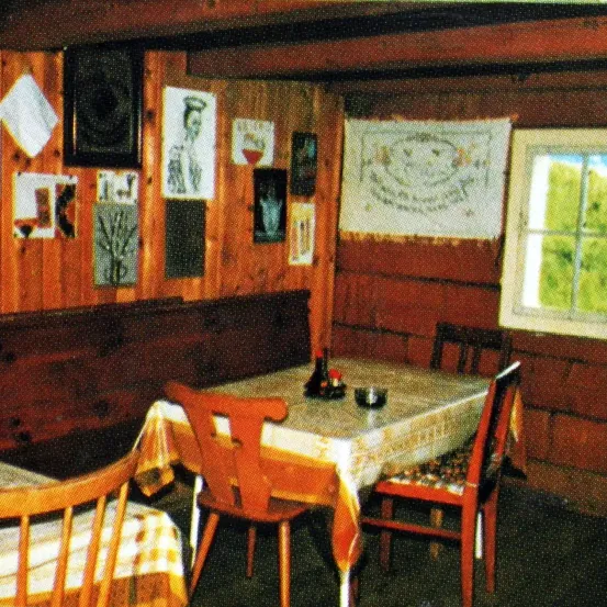 Ein kleiner Essbereich mit Holzmöbeln, einem mit Stoff bedeckten Tisch und verschiedenen Gegenständen an der Wand, einschließlich eines gerahmten Porträts.