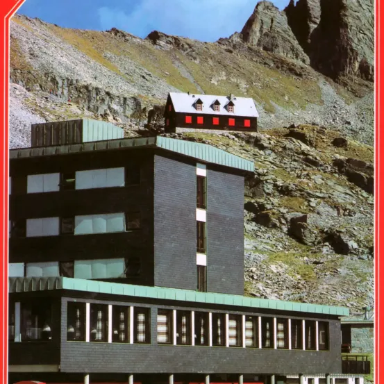 Ein modernes, mehrstöckiges Gebäude mit vielen Fenstern und einem kleineren Haus auf einem felsigen Berg.