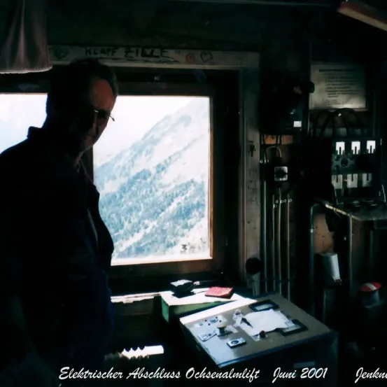 Ein Mann mit Brille schaut aus einem Fenster eines kleinen Raumes mit einem Schreibtisch und Bergen im Hintergrund. Es wurde im Juni 2001 aufgenommen.