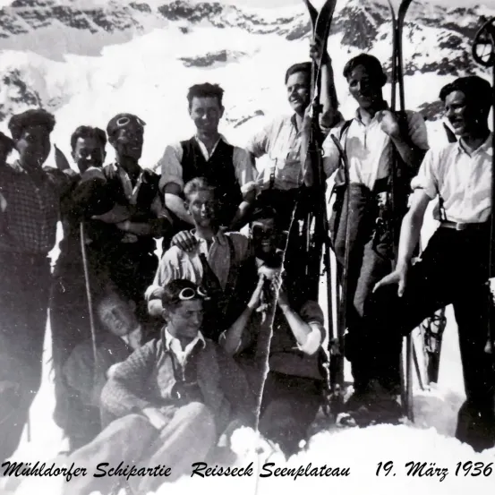 Ein Schwarz-Weiß-Foto einer Gruppe von Männern in Winterkleidung, die am 19. März 1936 im Schnee stehen und sitzen.