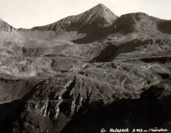 Ein Schwarz-Weiß-Foto eines bergigen Geländes. Es zeigt raue Gipfel und steile Hänge mit sichtbaren Erosionsspuren. Die Berge sind kahl, ohne Vegetation.