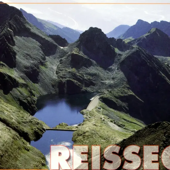 Luftaufnahme eines Gebirgsgeländes mit einem See und einem Damm. Die Berge sind mit Grünpflanzen und Felsen bedeckt. Das Wort 'REISSECO' ist in großen Buchstaben unten angezeigt.