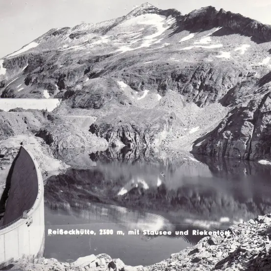 Schwarz-Weiß-Foto einer Bergkette mit einem See und Damm auf 2500 Metern über dem Meeresspiegel.