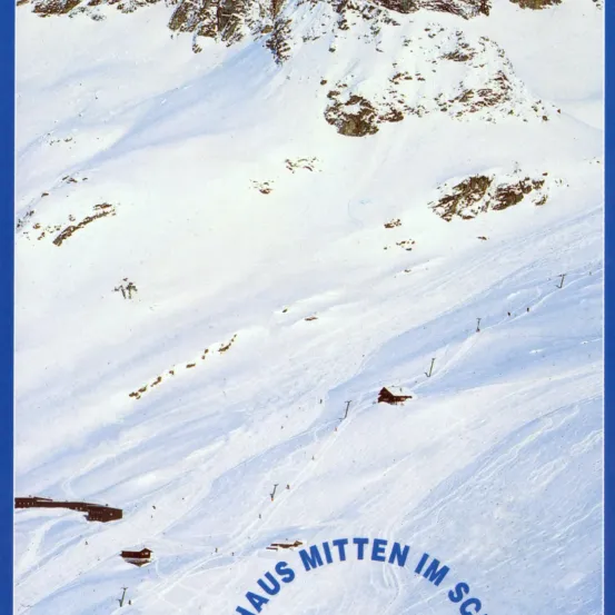 Eine verschneite Berglandschaft mit rauem Gelände und einer kleinen Hütte. Die Szene spielt sich in einer Gebirgsregion ab, wahrscheinlich in einem Skigebiet.