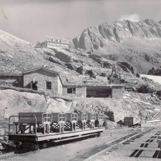 Ein Schwarz-Weiß-Foto eines Straßenbahnwagens auf einer Bergstrecke, mit einem Haus im Hintergrund und Bergen in der Ferne.