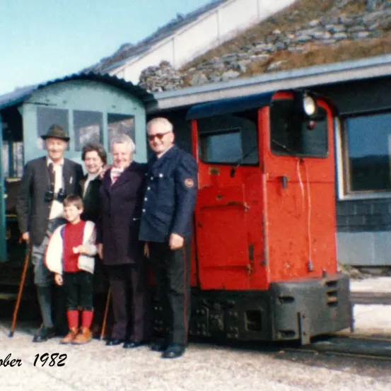 Eine Familie mit fünf Personen, darunter ein Kind, steht 1982 vor einer roten Zugkabine.