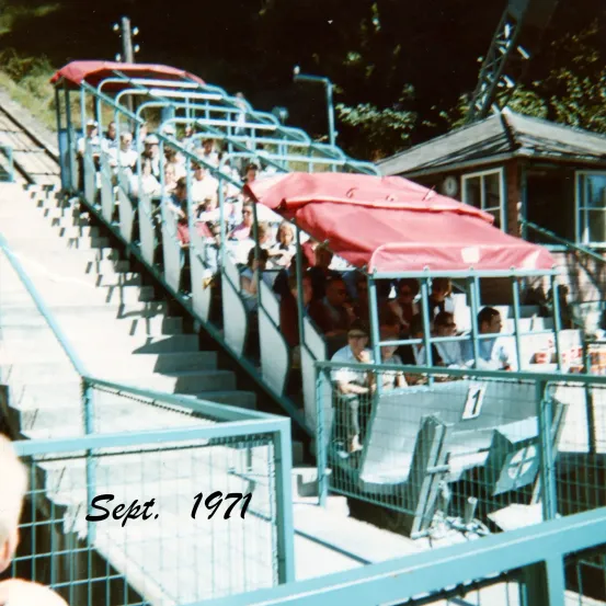 Ein Vintage-Foto von September 1971 zeigt eine Gruppe von Menschen, die eine rot-bedachte Gondel auf einer Treppe fahren, datiert in der unteren linken Ecke.
