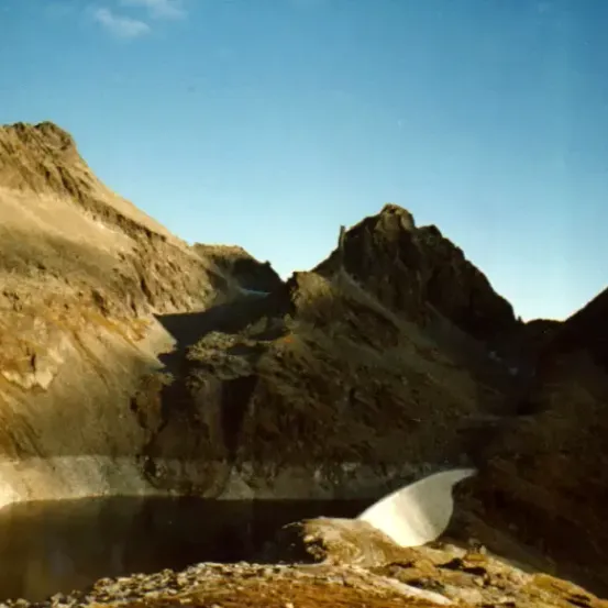 Eine Landschaft mit einem Berg und einem See an seiner Basis, unter einem klaren blauen Himmel.
