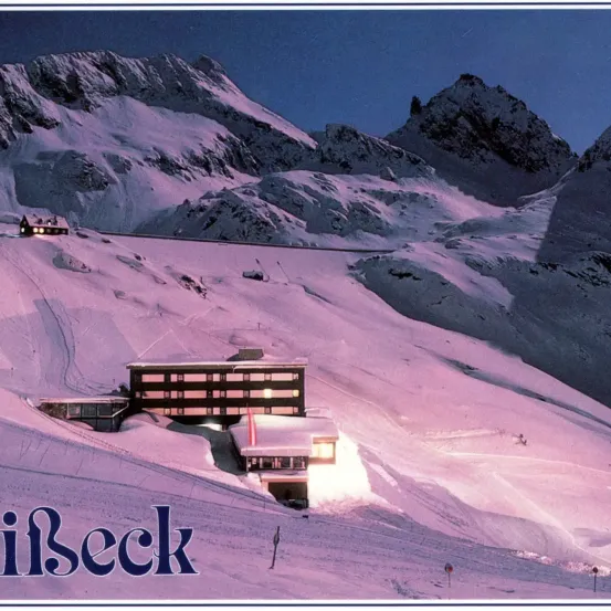Eine schneebedeckte Berglandschaft mit einem Skiresortgebäude im Vordergrund, beleuchtet in der Dämmerung oder Morgendämmerung. Das Bild hat einen lila Farbton und zeigt das Wort 'Innseck' in großen Buchstaben am unteren Rand.