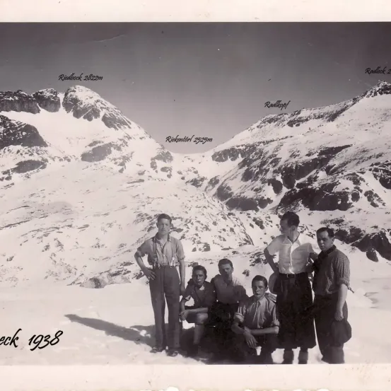 Schwarz-Weiß-Foto von fünf Männern, die 1938 vor verschneiten Bergen stehen. Die Höhen der Berge sind markiert.