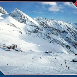 Eine verschneite Berglandschaft mit Skifahrern und Skiliften. Gebäude sind im Schnee eingebettet. Der Himmel ist blau mit einigen Wolken.