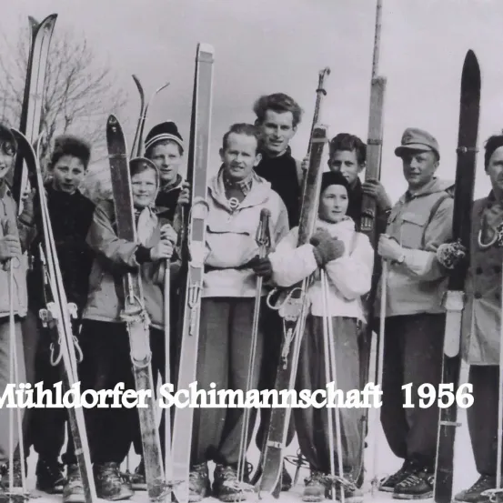 Eine Gruppe von Menschen, die zusammenstehen und Skier in der Hand halten, das Bild ist auf das Jahr 1956 datiert und zeigt ein Wintersportteam.