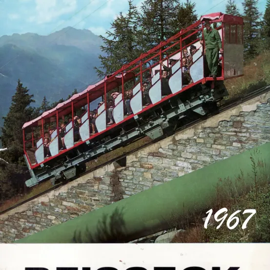 Eine rote und weiße Seilbahn aus dem Jahr 1967 erklimmt eine steile Bergstrecke, umgeben von Bäumen und Bergen.