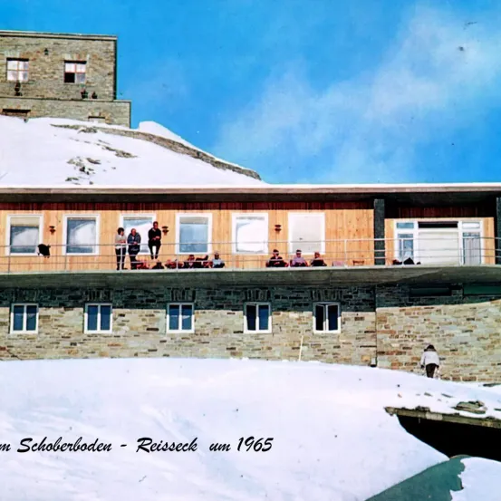 Ein schneebedecktes Gebäude mit mehreren Personen auf dem Balkon. Das Gebäude befindet sich in Schoberboden-Reisseck. Um 1965 datiert.