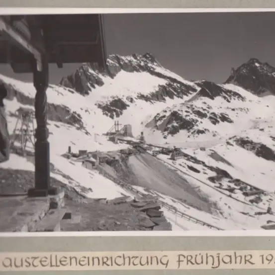 Ein Schwarz-Weiß-Foto einer Bergregion im frühen Frühling 1953, mit einer Holzstruktur und einer Person in der Nähe.