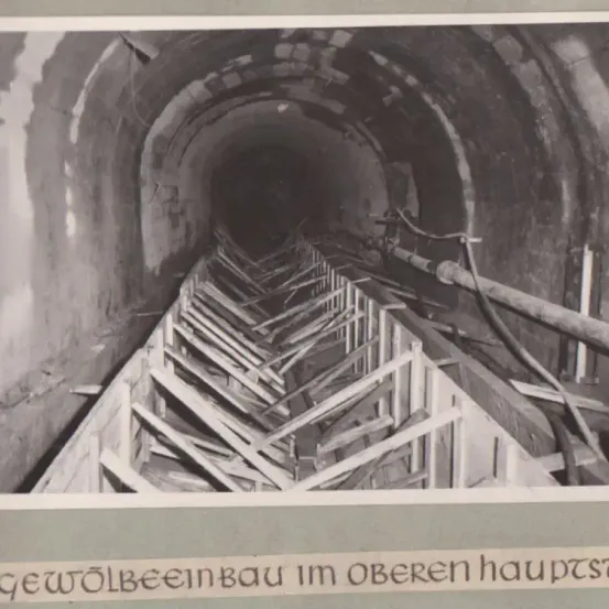 Ein Foto zeigt einen Tunnel mit gewölbter Decke und Stützbalken, möglicherweise im Bau oder in der Wartung.