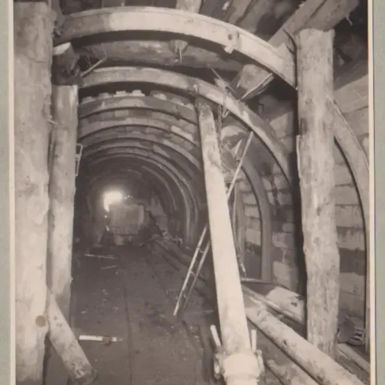 Ein Schwarz-Weiß-Foto eines alten, verlassenen Tunnels mit Holzstützen und einem Licht am Ende.