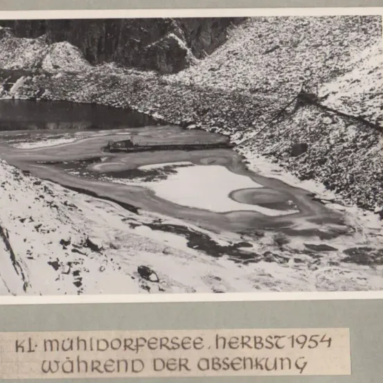 Schwarz-Weiß-Foto von Muhi Dorfsee, aufgenommen im Herbst 1954 während einer Zeit des Wasserrückgangs. Das Bild zeigt eine Landschaft mit einem Fluss und felsigem Gelände.