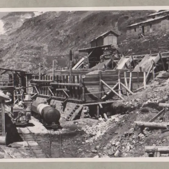 Ein Schwarz-Weiß-Foto einer Bergbauoperation an einem Berghang mit Holzgebäuden und Gleisen.