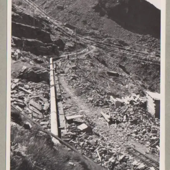 Ein Schwarz-Weiß-Foto zeigt einen Berg mit Schutt, einer beschädigten Eisenbahnstrecke und einem kleinen Gebäude auf der rechten Seite.