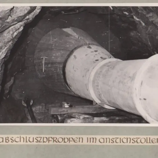 Eine große Rohrleitung ist in einem Tunnel befestigt, mit einem Hammer und Felswänden. Der Text darunter lautet 'abschluszpropfen im ansichstoler'.