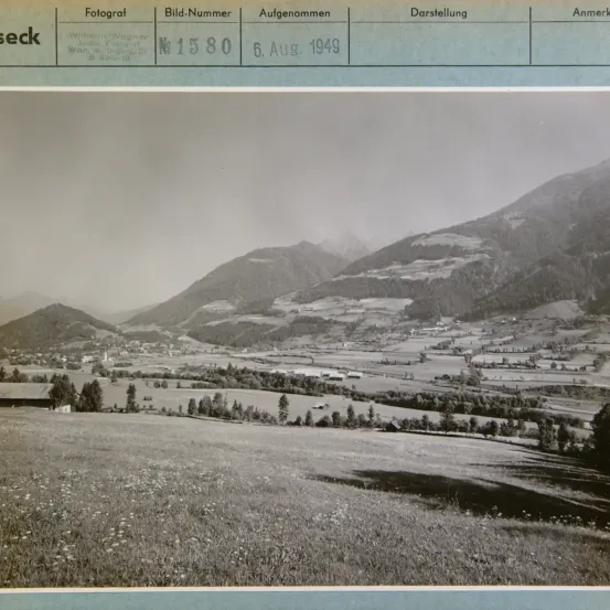 Ein Foto mit der Bezeichnung 'Fotograf' und der Nummer '1580'. Das Foto wurde am 6. August 1949 aufgenommen. Es zeigt eine Landschaft mit Bergen, einem Tal und einigen Bäumen.