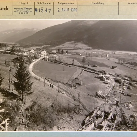 Schwarz-Weiß-Foto einer Berglandschaft mit einer Straße, Gebäuden und einer Eisenbahnstrecke. Das Bild hat einen Wasserzeichen mit der Aufschrift 'Wilhelm Wagner techn. Fotograf' und 'Wien, III. Ungar. 27'. Das Foto wurde am 2. April 1949 aufgenommen.