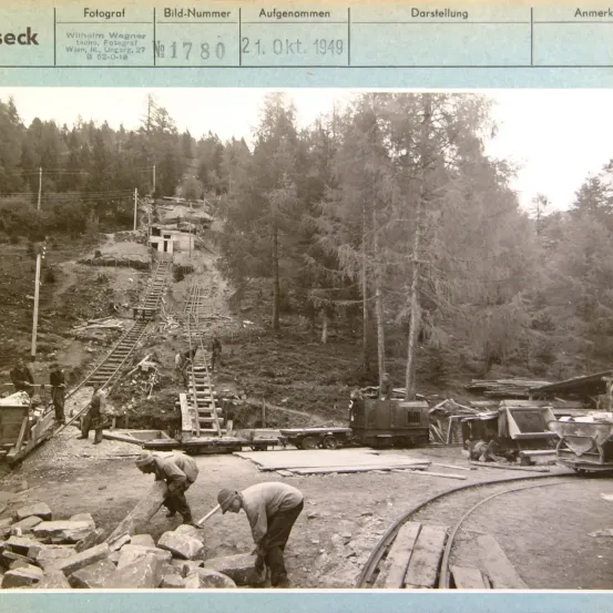 Schwarz-Weiß-Foto von Arbeitern beim Bau einer Eisenbahn in einem Wald, aufgenommen am 21. Oktober 1949. Das Bild enthält eine Bildnummer und eine Bildunterschrift.