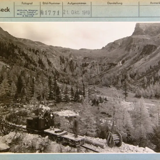 Ein altes Foto zeigt eine Berglandschaft mit einer kleinen Bahn auf einer Bahnstrecke. Es wurde am 21. Oktober 1949 von Wilhelm Wagner aufgenommen.