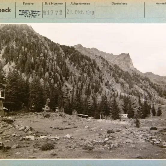 Schwarz-Weiß-Foto mit der Bezeichnung 'Fotograf Wilhelm Wagner', das eine Berglandschaft mit mehreren kleinen Gebäuden zeigt. Das Foto ist vom 21. Oktober 1949.