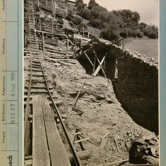 Schwarz-Weiß-Foto zeigt eine eingestürzte Eisenbahnbrücke mit Holzgerüst und rauem Gelände.